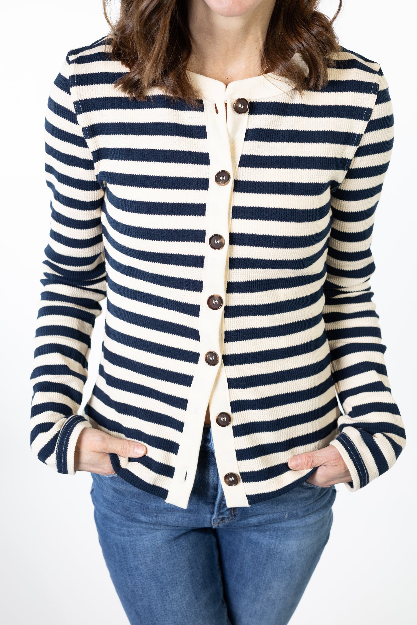 Person wearing a navy and white striped cardigan with blue jeans on a white background