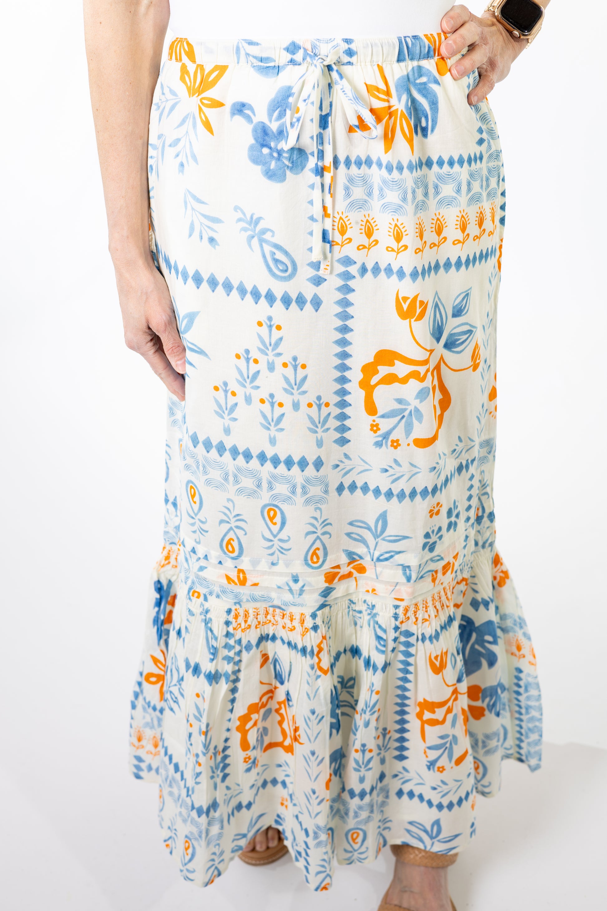 Person wearing a long, patterned skirt with blue and orange designs on a white background