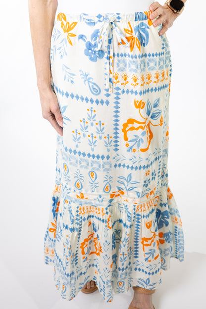 Person wearing a long, patterned skirt with blue and orange designs on a white background