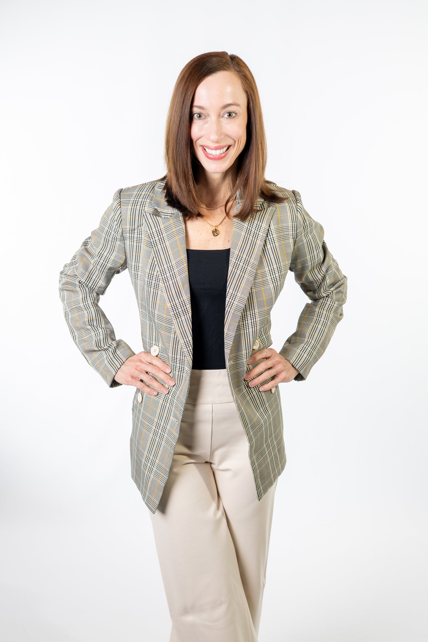 Woman wearing a plaid blazer over a black top and beige pants on a white background