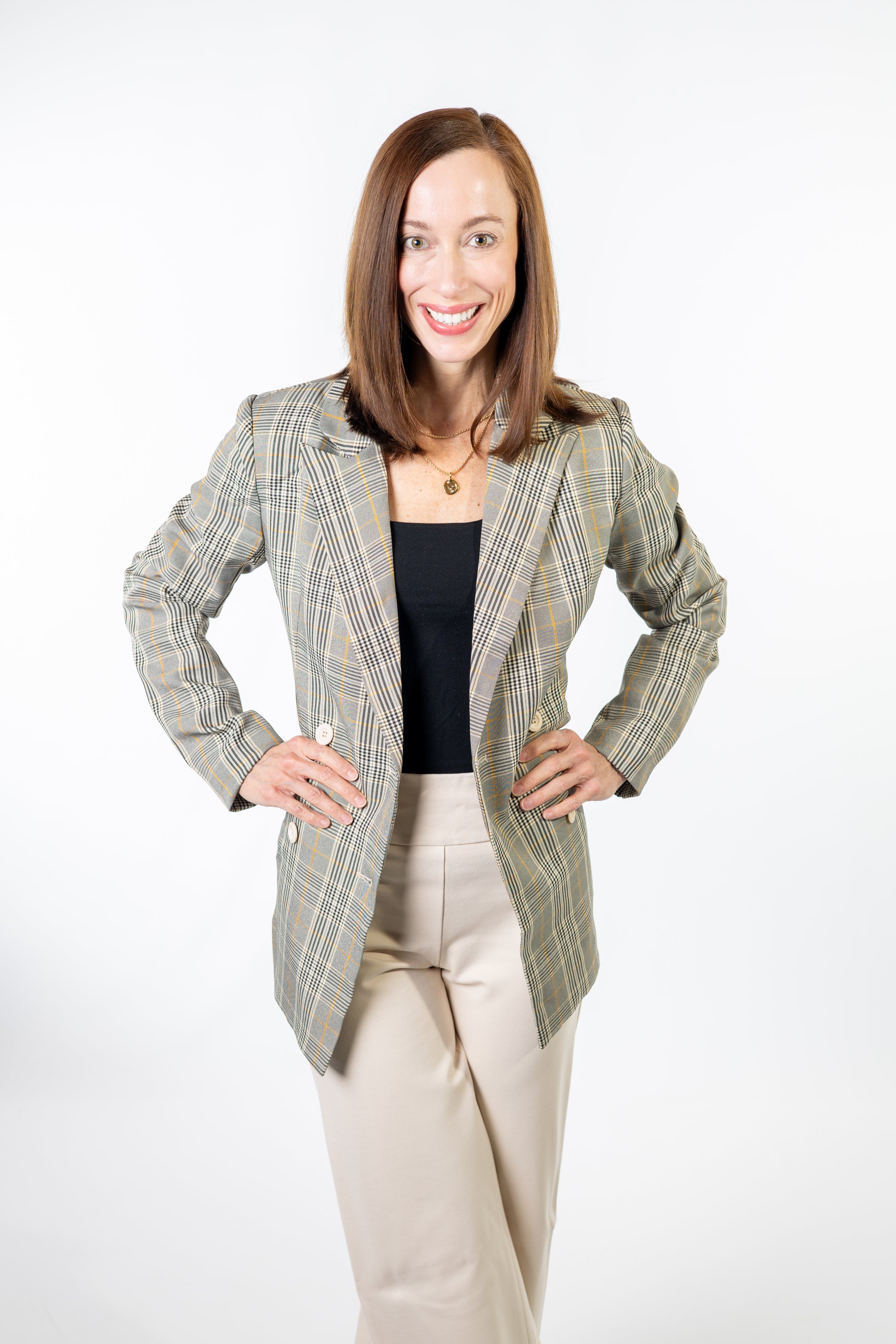 Woman wearing a plaid blazer over a black top and beige pants on a white background