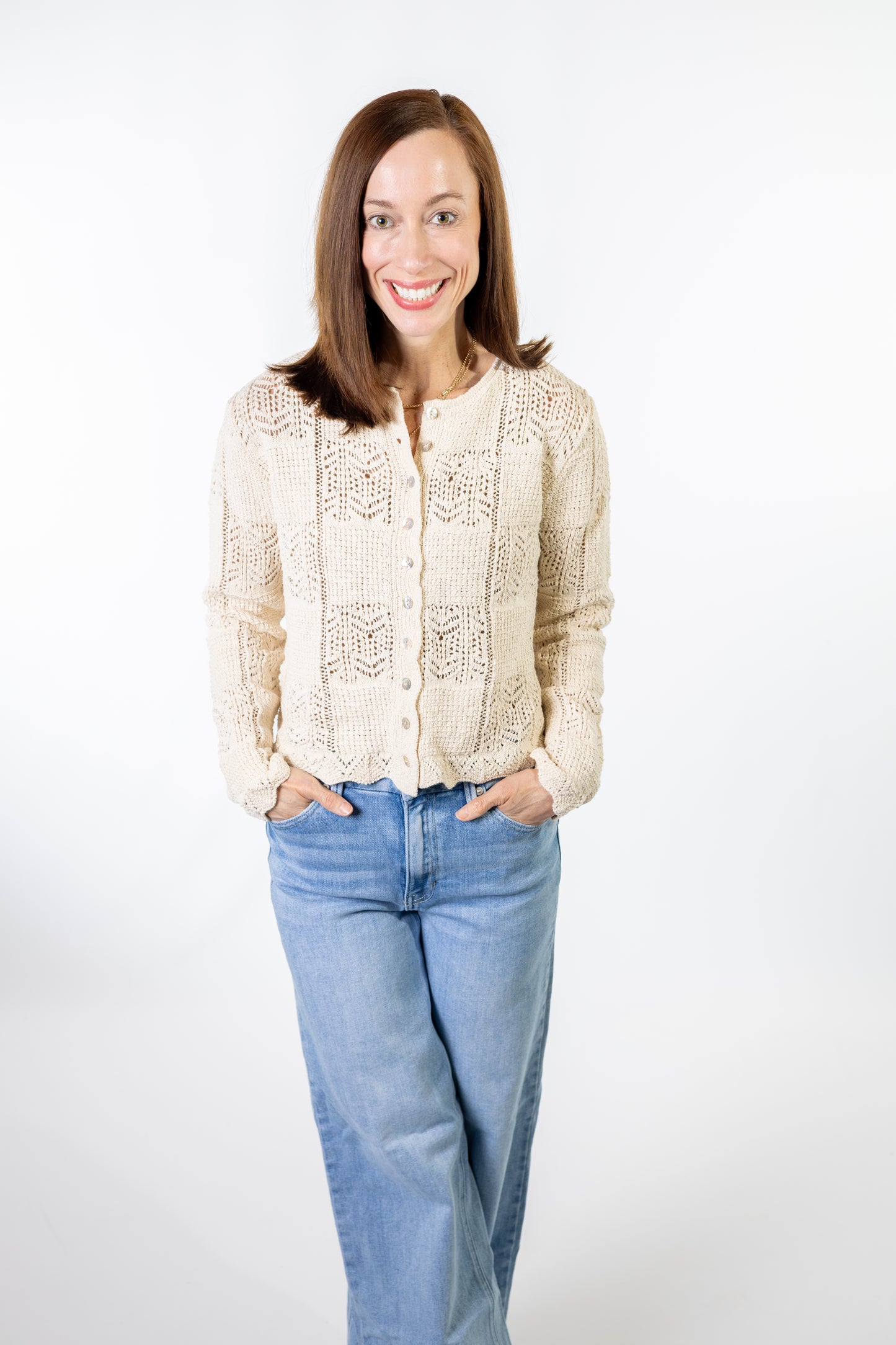 Woman wearing a cream lace crochet cardigan and blue jeans on a white background