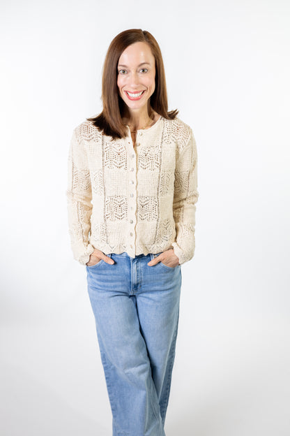 Woman wearing a cream lace crochet cardigan and blue jeans on a white background