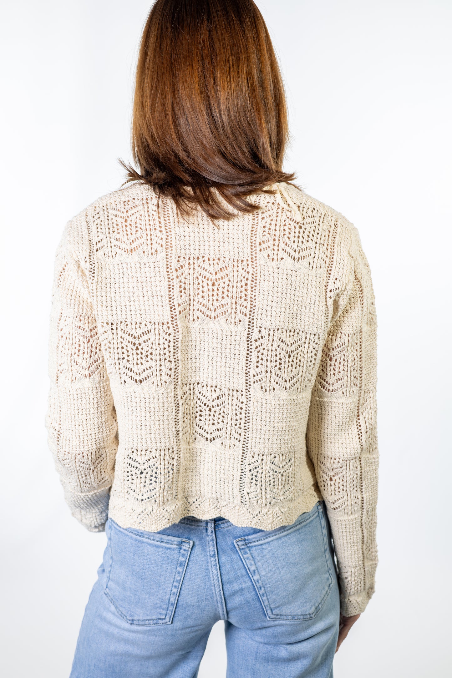 Person wearing a beige natural lace crochet cardigan and light blue jeans on a white background