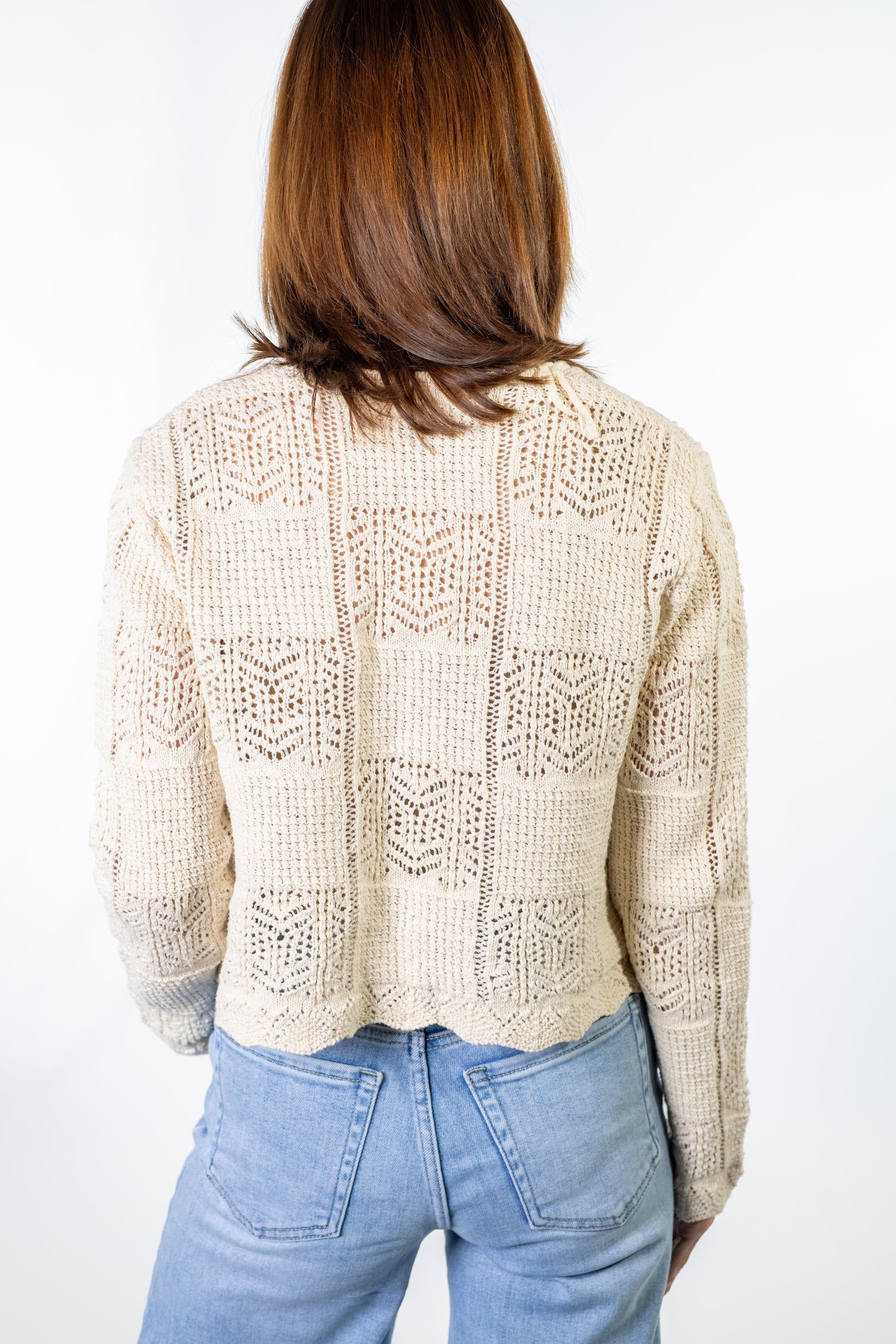 Person wearing a beige natural lace crochet cardigan and light blue jeans on a white background