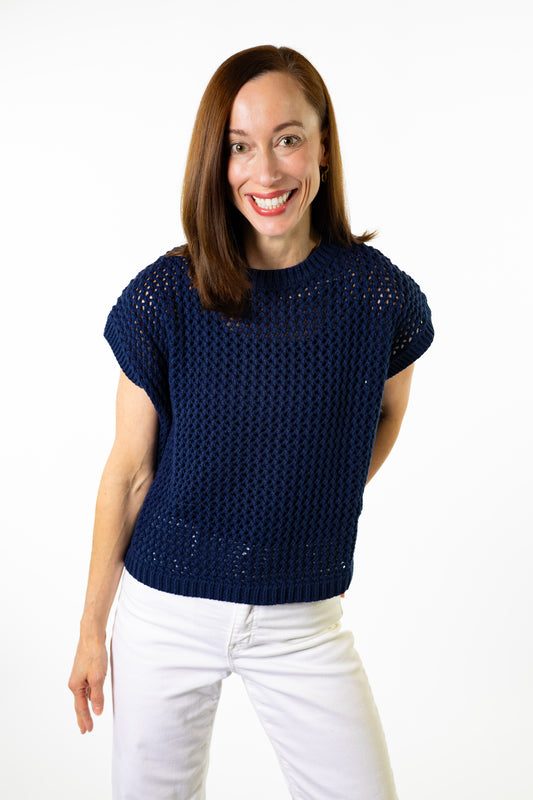woman wearning navy blue open knit sweater with short sleeves, wearing white pants and white background