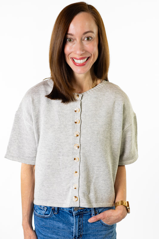 Woman wearing a light gray button-up shirt and blue jeans on a white background