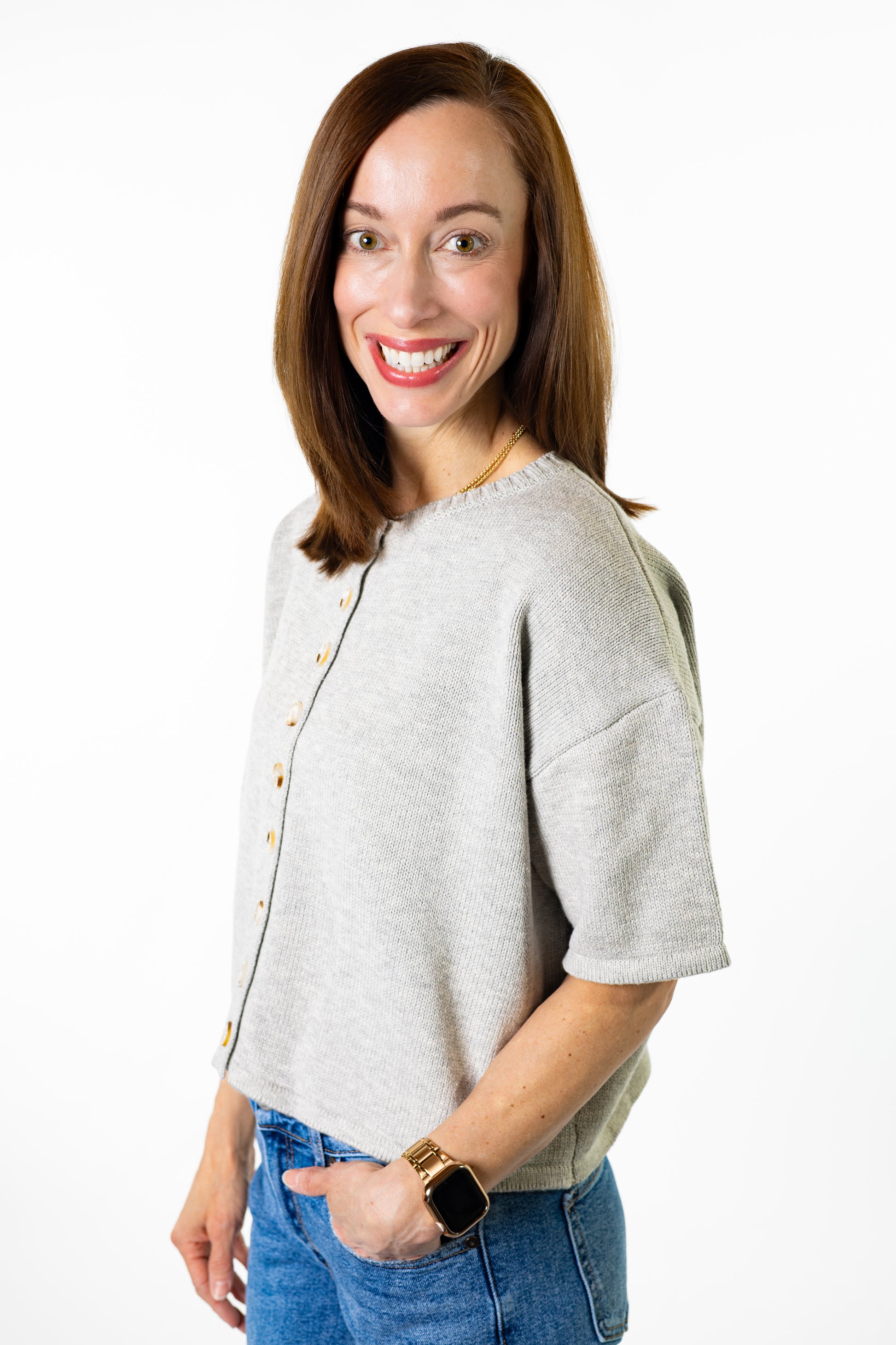 Woman wearing a light gray button cardigan short sleeves with buttons and blue jeans on a white background