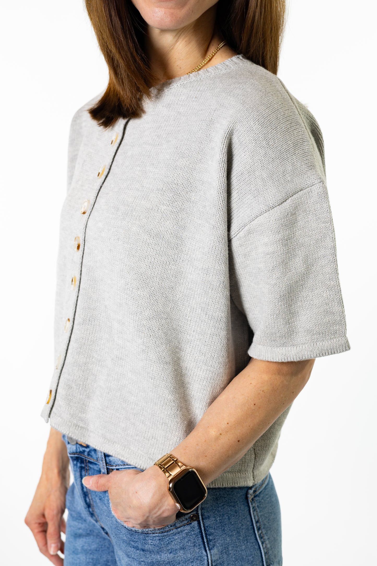 Person wearing a light gray sweater with button details on a white background