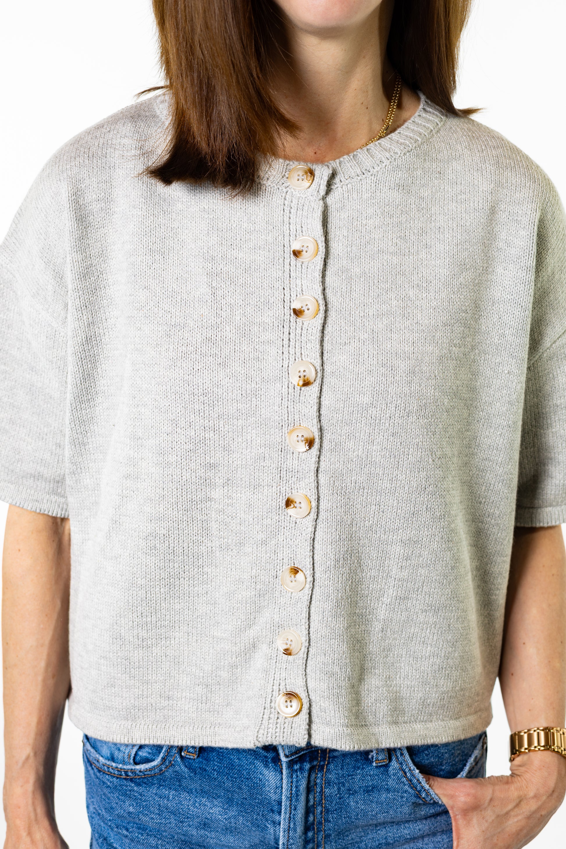 Person wearing a light gray button-up shirt with a white background