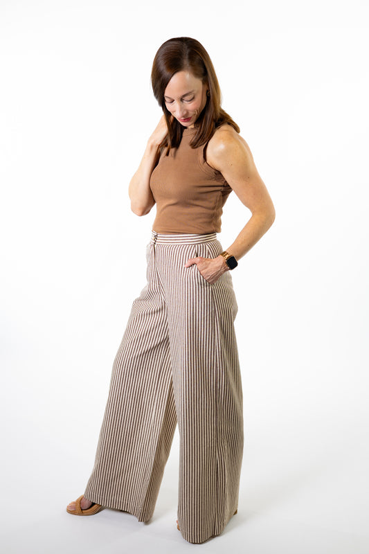 Woman wearing a brown top and brown striped pants on a white background