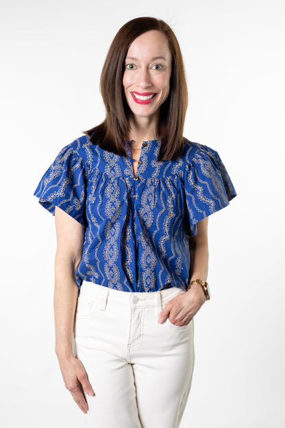 Woman wearing a blue patterned blouse and white pants on a white background