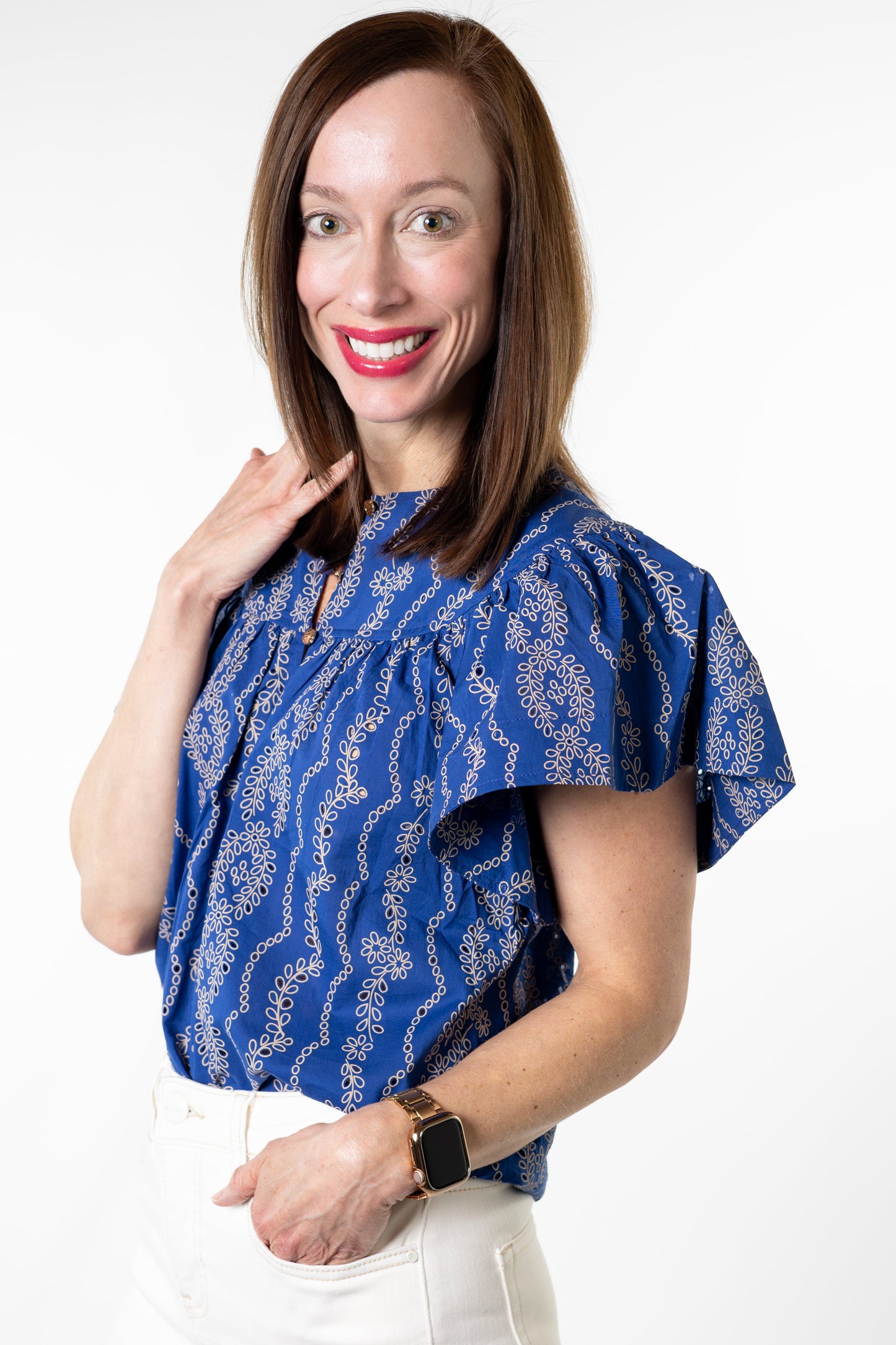 Woman wearing a blue patterned blouse and white pants on a white background