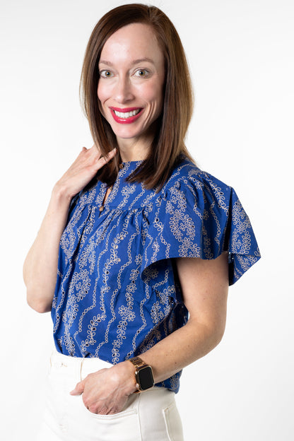 Woman wearing a blue patterned blouse and white pants on a white background