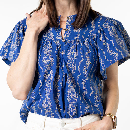 Woman wearing a blue patterned blouse and white pants on a white background