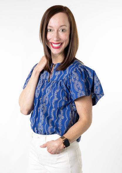 Woman wearing a blue patterned blouse and white pants on a white background