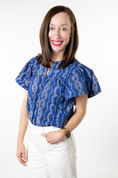 Woman wearing a blue patterned blouse and white pants on a white background