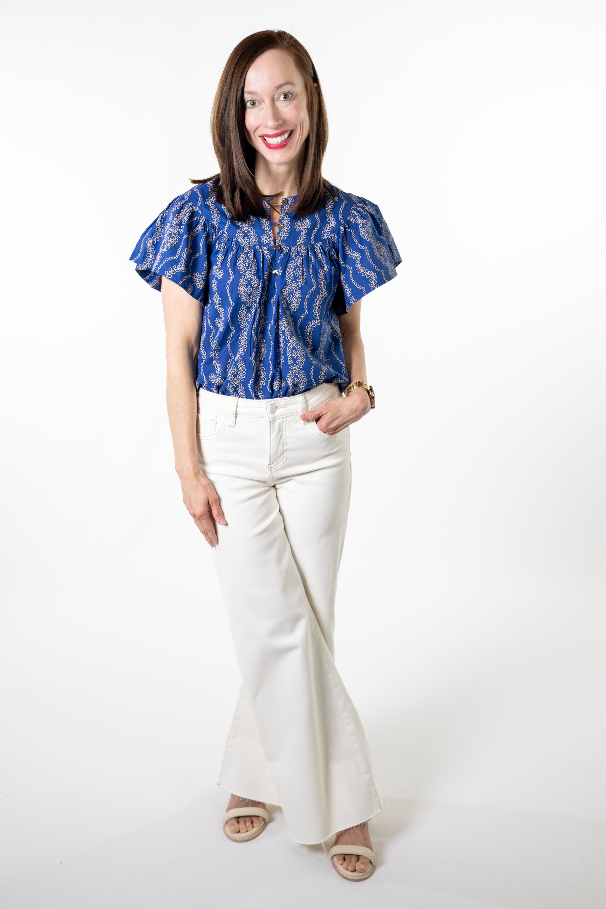 Woman wearing a blue patterned top and white pants on a white background