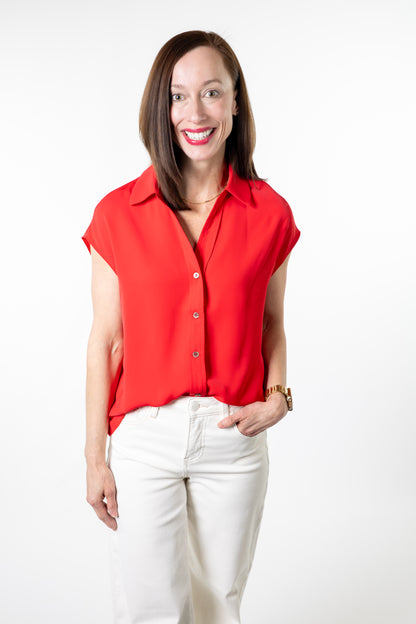 Woman wearing a red cap sleeve shirt blouse and white pants on a white background
