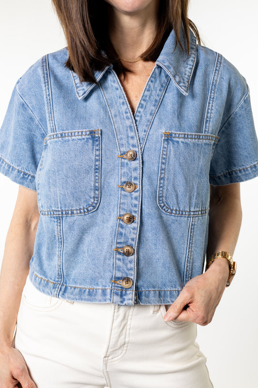 Person wearing a light blue denim button shirt jacket with a plain background