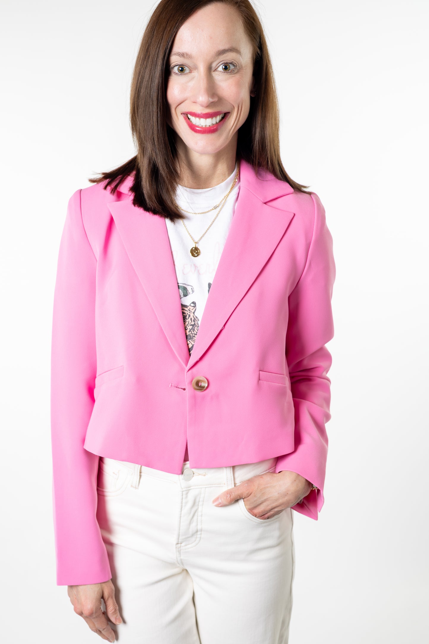 Woman wearing a pink blazer over a white top with a pattern, on a white background