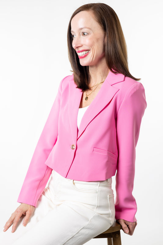 Woman wearing a pink blazer and white pants on a white background