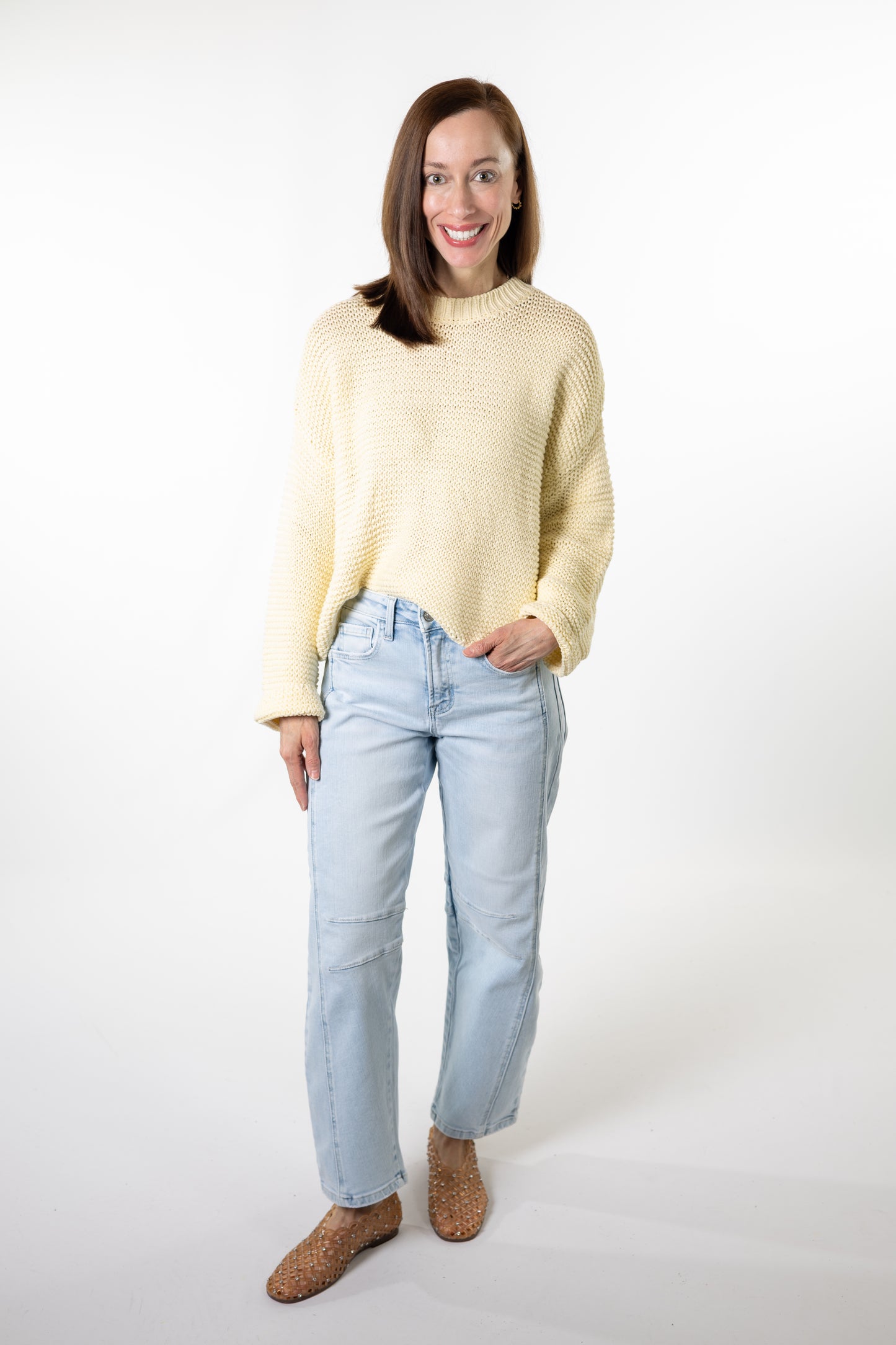 Woman wearing a light yellow sweater and light blue jeans on a white background