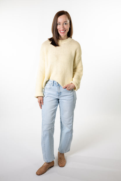 Woman wearing a light yellow sweater and light blue jeans on a white background