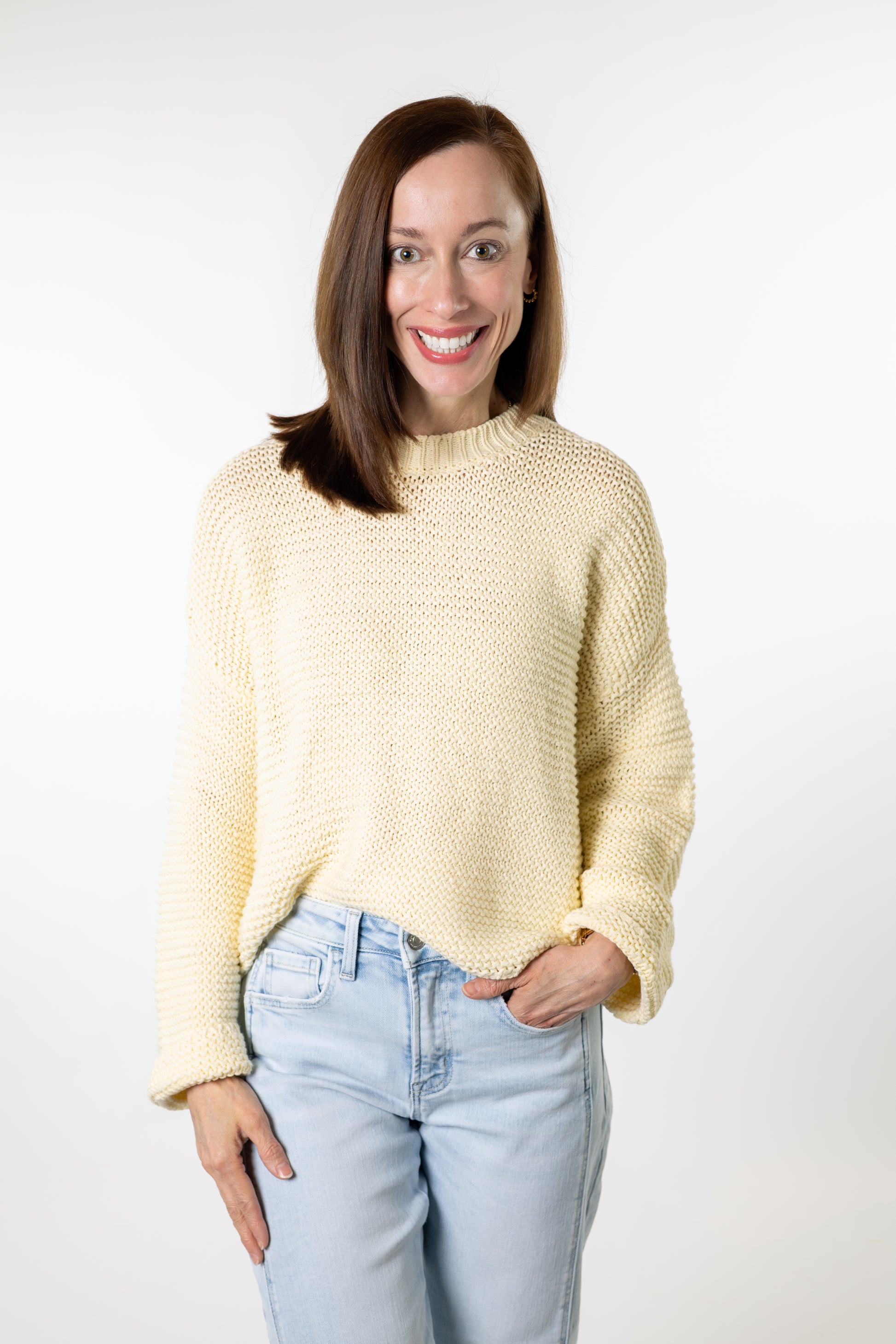 Woman wearing a light yellow sweater and light blue jeans against a white background