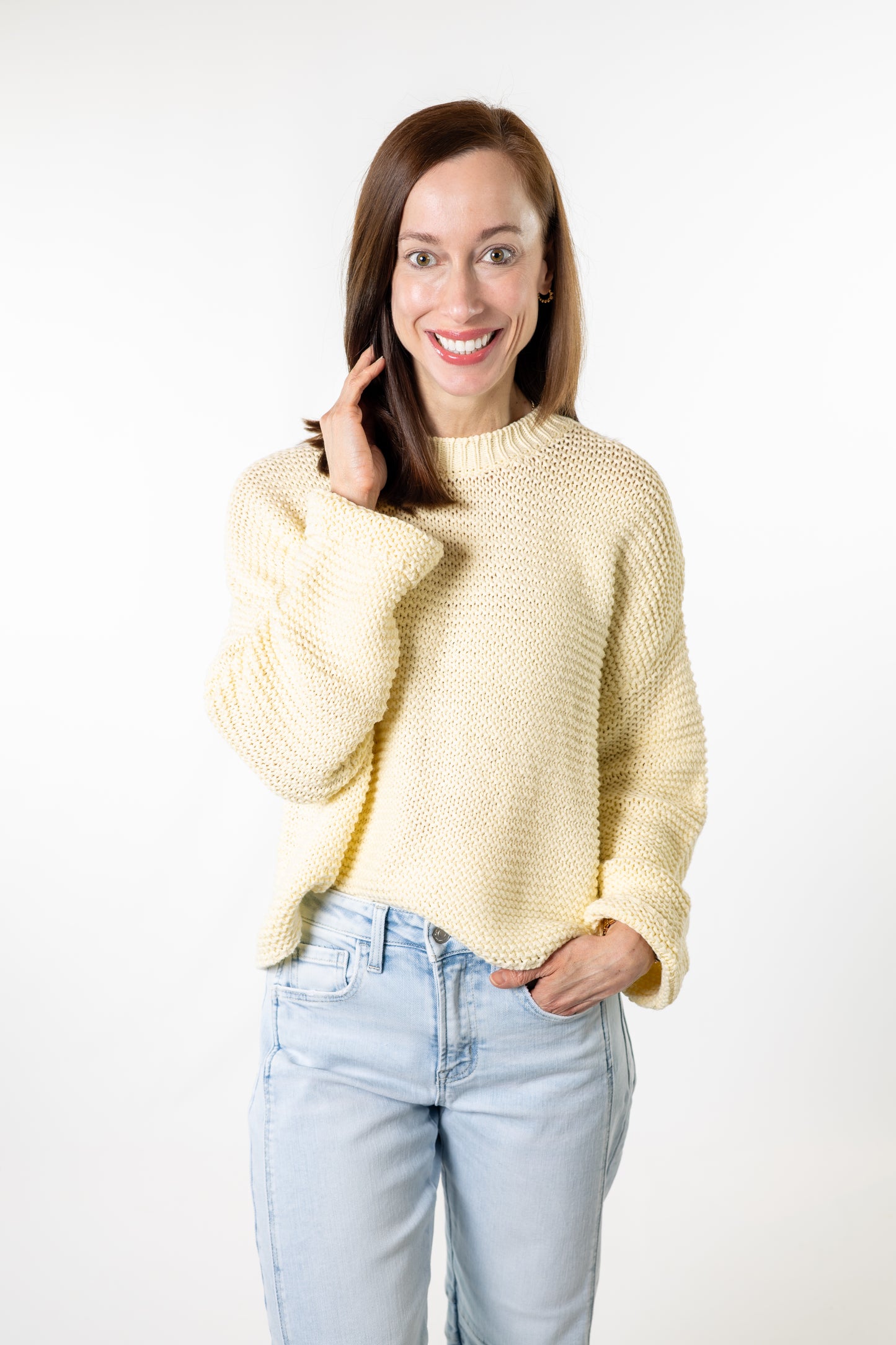 Woman wearing a light yellow sweater and light blue jeans on a white background
