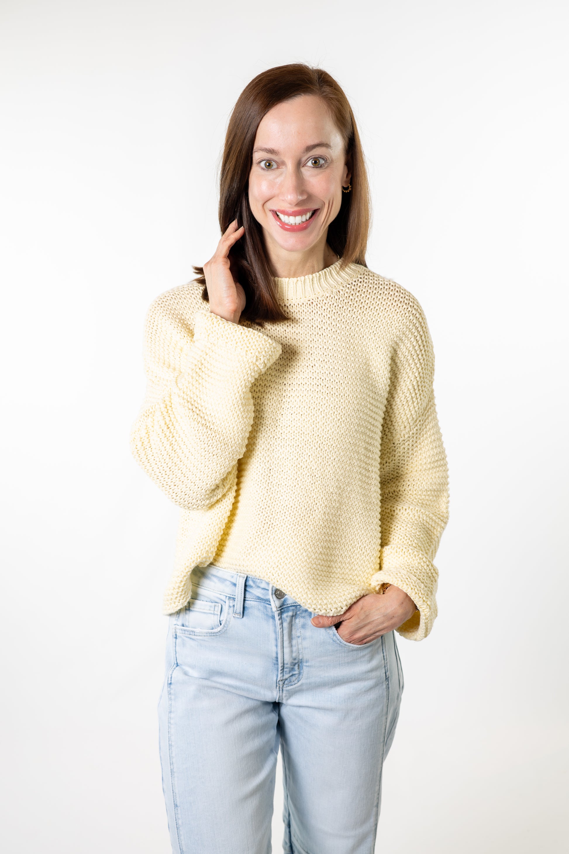 Woman wearing a light yellow sweater and light blue jeans on a white background