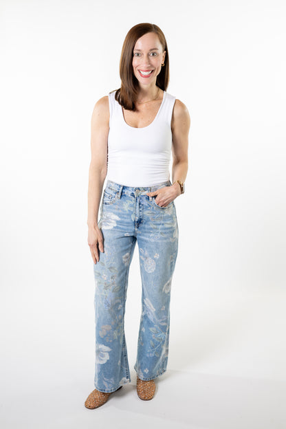 Woman wearing a white tank top and light blue jeans with floral patterns on a white background