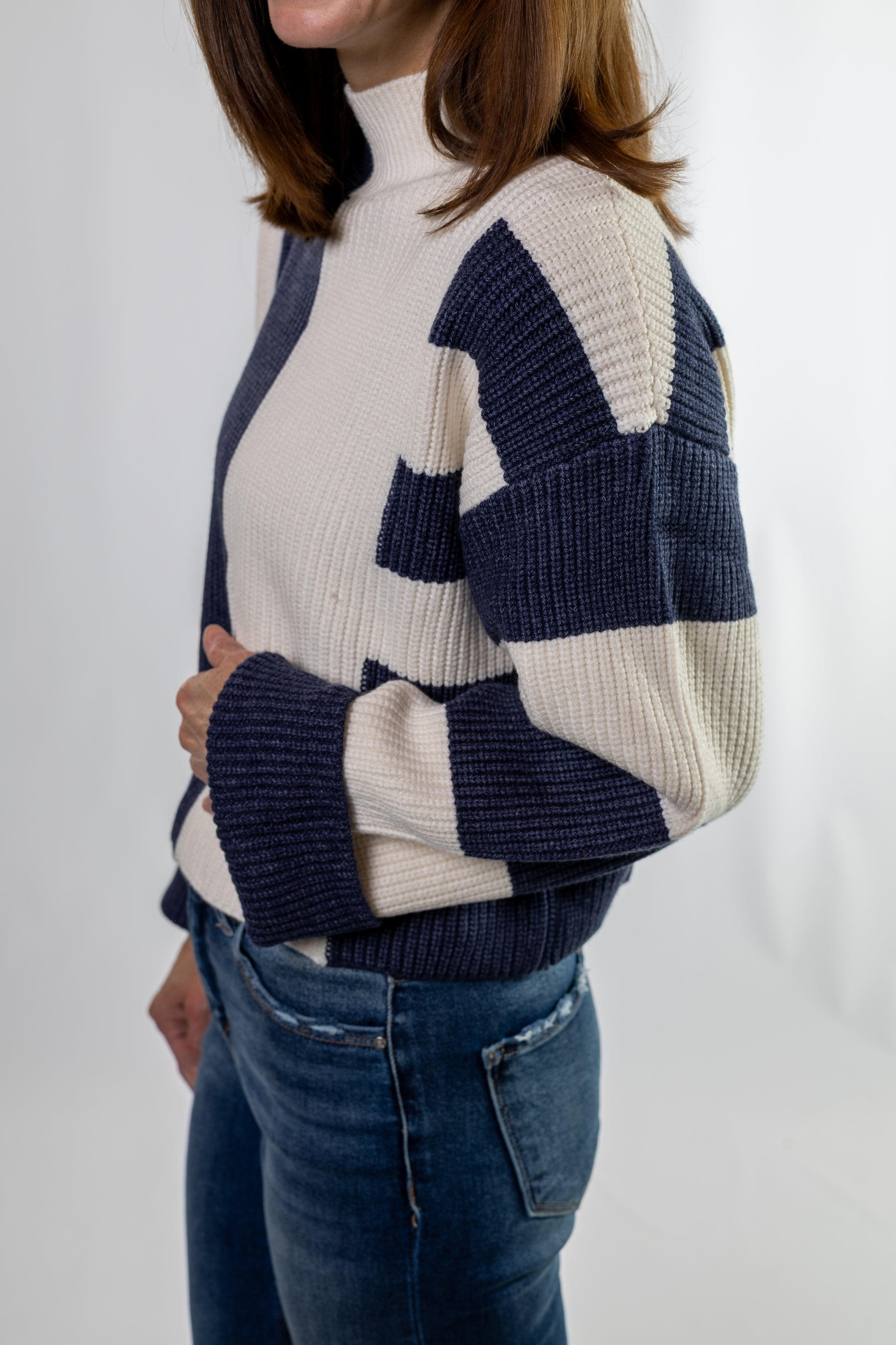 Person wearing a white and blue patterned sweater with jeans on a plain background