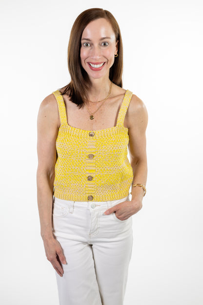 Woman wearing a yellow sleeveless top with buttons and white pants on a white background