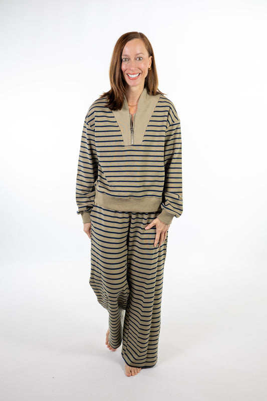 A woman modeling a matching two-piece loungewear set consisting of a long-sleeve quarter-zip sweatshirt and wide-leg pants, both in green and navy striped pattern, against a plain white studio background.