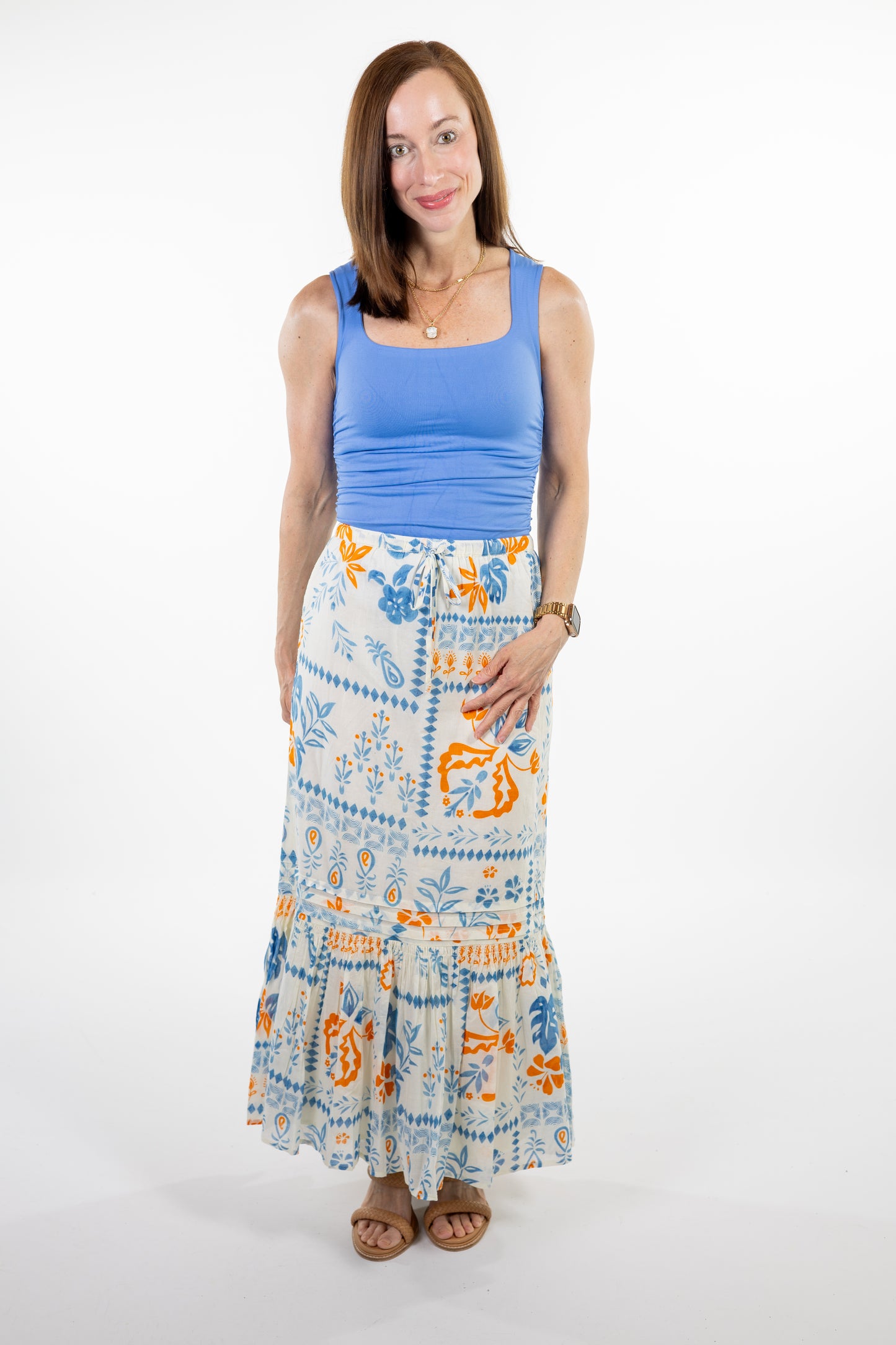 Woman wearing a blue tank top and a long, patterned skirt on a white background