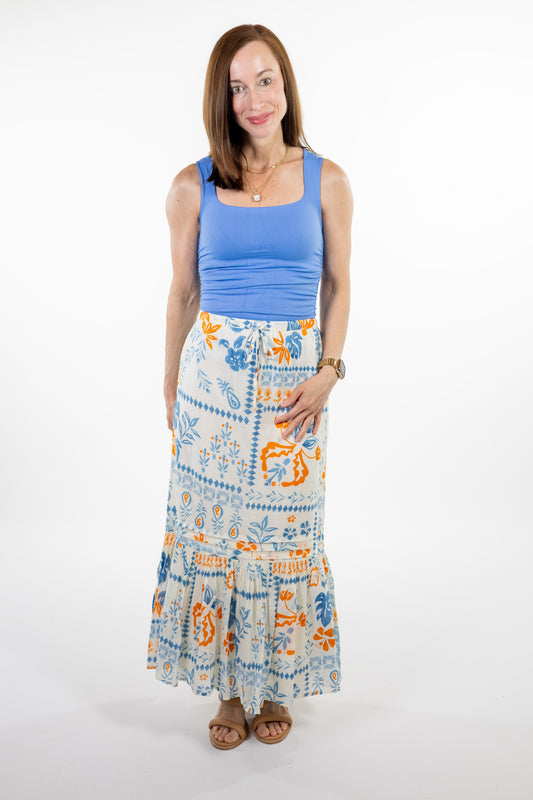 Woman wearing a blue tank top and a long, patterned skirt on a white background