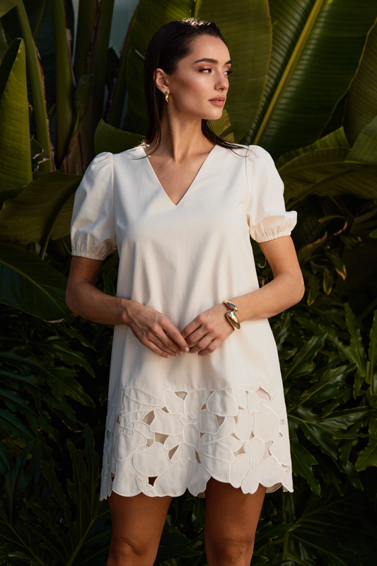 Woman wearing a white dress with leaf patterns against a green leafy background