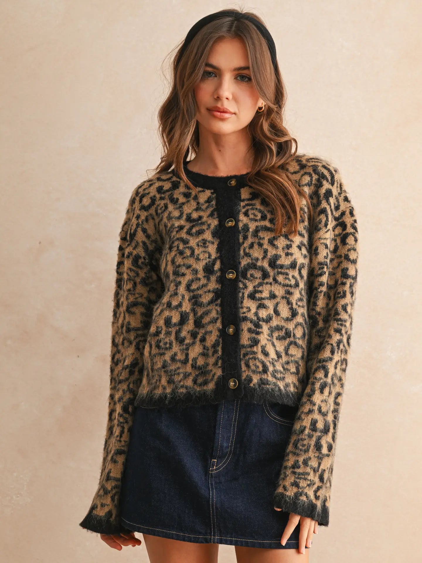 Woman wearing a leopard print cardigan over a black top with a denim skirt on a beige background
