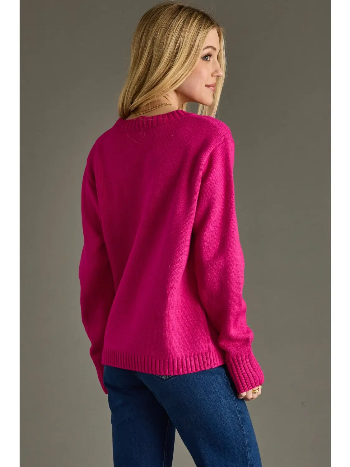 Woman wearing a bright pink sweater and blue jeans against a gray background