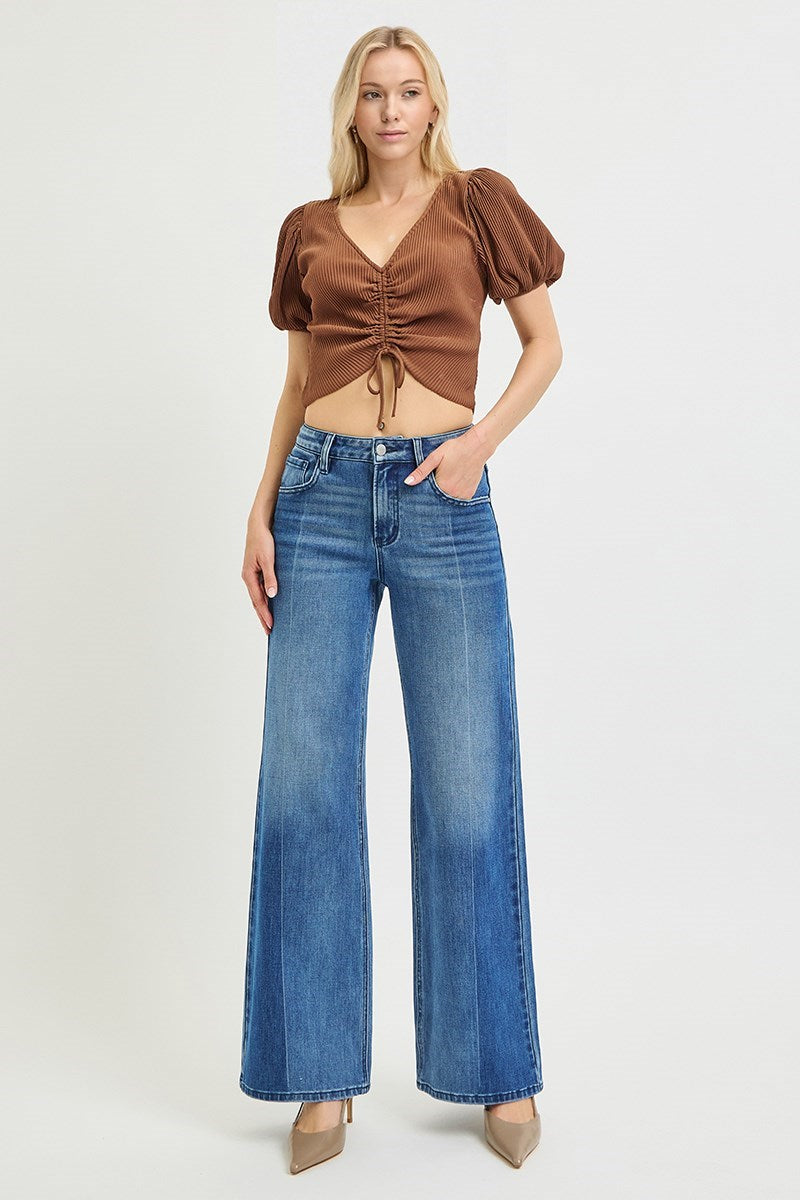 Woman wearing a brown top and blue jeans on a white background