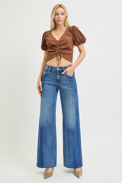 Woman wearing a brown top and blue jeans on a white background
